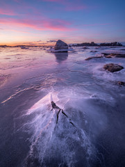 A single rock breaks through the sheet of ice over the sea in the Swedish archipelago.