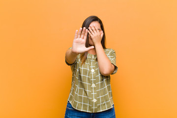 young pretty woman covering face with hand and putting other hand up front to stop camera, refusing...