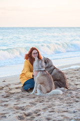 red-haired girl in a yellow rain coat and two husky dogs on the beach