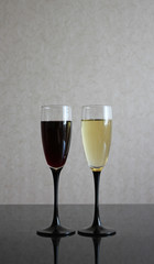 Two wineglasses with white and red wine on black glass table. Gray blurred wall behind. Background with dark and light liquids in goblets.