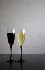 Two wineglasses with white and red wine on black glass table. Gray blurred wall behind. Background with dark and light liquids in goblets and place for text.