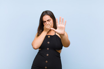young pretty woman covering face with hand and putting other hand up front to stop camera, refusing...