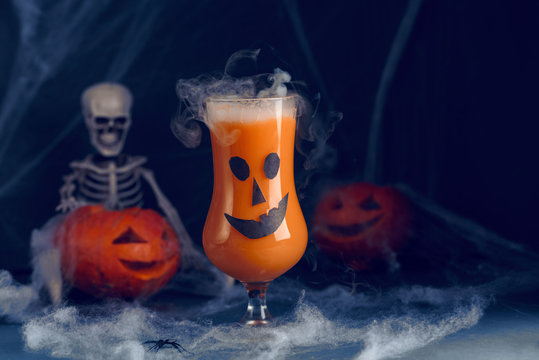 Halloween Orange Drink In Ghost Glasses With Skeleton, Pumpkin And Smoke