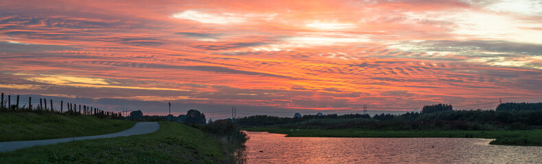 Stunning panorama of dutch landscape with road along the waterside below a vibrant pink sky