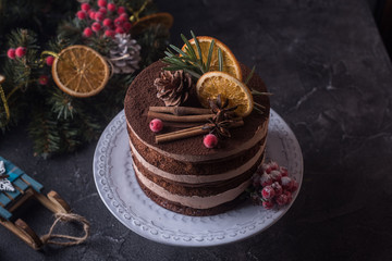 Rustic chocolate Christmas cake decorated cinnamon and orange slice on black table with Christmas attributes