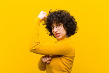 young pretty afro woman feeling happy, satisfied and powerful, flexing fit and muscular biceps,...