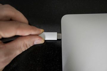 Male hand plugging white USB-C Type C cable into a port on a grey laptop notebook computer. USB type-C port and Cable's White of laptop.