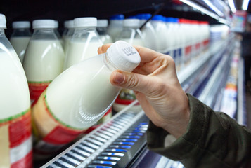 Womans hand holding milk bottle in supermarket. Man shopping milk in grocery store. Man checks...