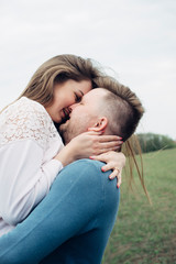 Young beautiful couple in love staying and kissing. Hugs together and smile spend good time on the green field and enjoy each. Lifestyle.