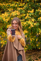 Attractive blonde is giving at camera coffee in the autumn park