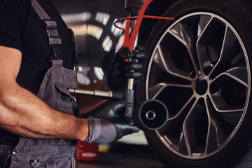 Fototapeta premium Muscular man is fixing car's wheel with special tool at auto service.