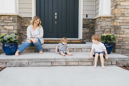 A Mother Sits With Her Sons On Her Front Steps Of Her Beautiful Home