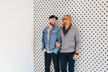 Interracial gay couple poses in front of a modern tile wall