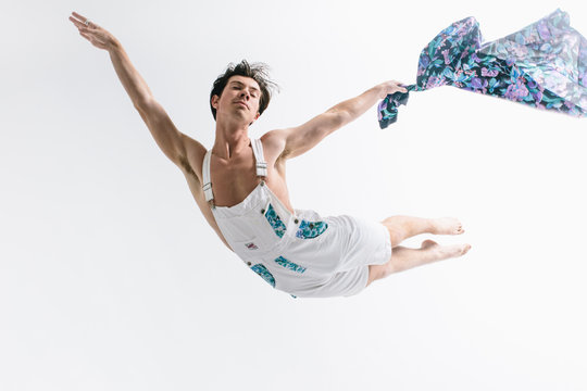 Male dancer in white denim overalls leaps into the air