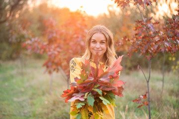 Beautiful blonde with an armful of leaves in autumn park