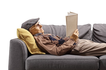 Elderly man lying on a couch and reading a book