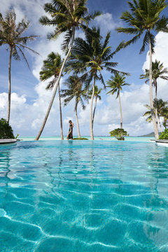 Woman walking by infinity pool on vacation at luxury resort