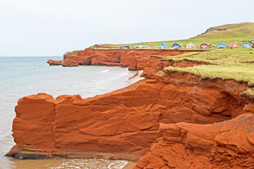 Fototapeta premium Eroded red sandstone cliffs and colorful cottages are typical of landscapes and seascapes in Canada's Madeleine Islands.
