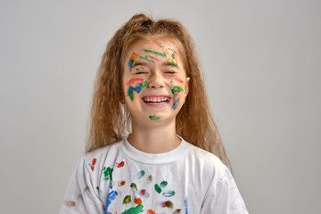 Little girl in white t-shirt, with painted face is making grimaces while posing isolated on white. Art studio. Close-up.