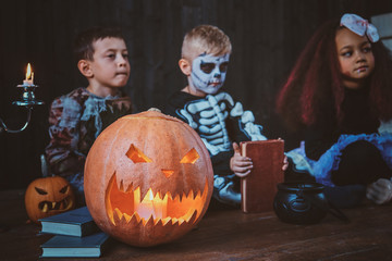 Good little friends in Halloween costumes are sitting on the floor with pumpkins and candles.