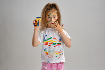 Little girl in white painted t-shirt, with colored face is playing with a sponge soaked in paint. Isolated on white. Close-up.