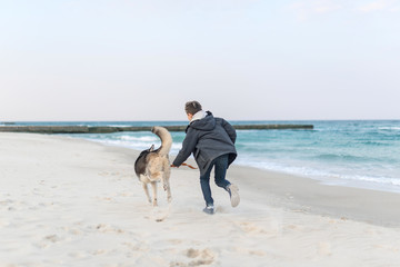 Back boy running with husky dog in collar on the beach