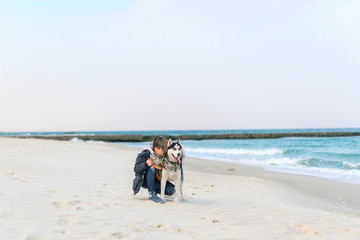 Boy sitting with husky dog on leash on the beach