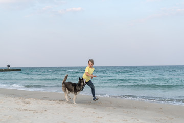 Boy running with husky dog in collar on the beach