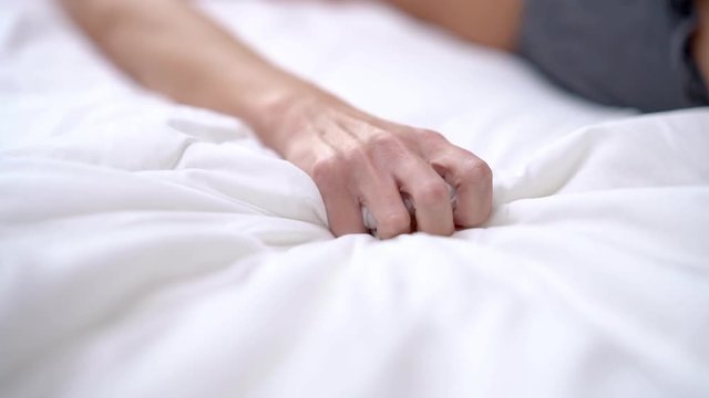 Woman's hand squeezing white sheet in erotic excitement