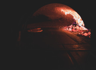 Toned dark photo of traditional oven for pizza with flame and pizza inside.