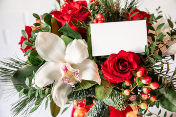 Beautiful flower arrangement of white orchid, red roses, natural spruce branches with card for text.
