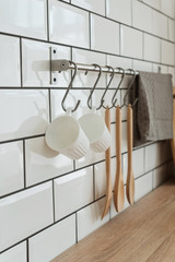 Two white cups, cutlery on hook and dishes in the white modern kitchen, organizing space