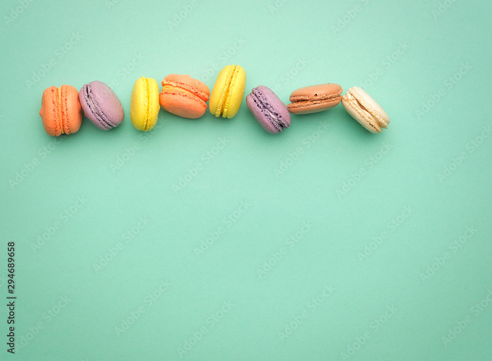 Poster round multi-colored baked macarons with cream lie in a line on a green background
