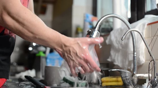 A man rinses previously washed and washed dishes to save water resources. Close-up of hands that rinse dishes underwater in the kitchen