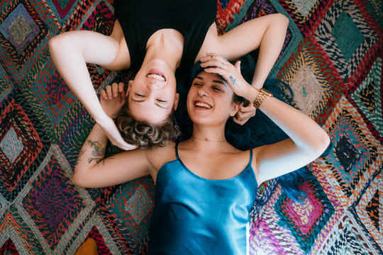 two lesbian girls lying and laughing on a colorful carpet
