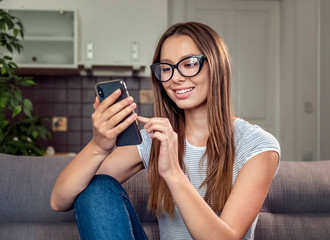 Fototapeta na wymiar Pretty brunette woman using smartphone sitting on sofa, indoors shot