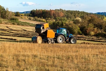 Fototapeta na wymiar Blue tractor packs straw. Autumn work on the farm. Tractor on the field. Ecological agriculture.