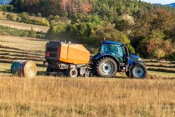Blue tractor packs straw. Autumn work on the farm. Tractor on the field. Ecological agriculture.