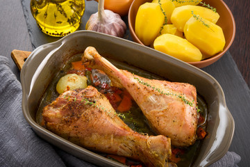 Roasted turkey legs in ceramic bowl with vegetables, potato and herbs