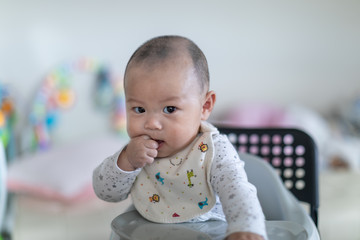 Cute baby sitting in a highchair chewing his finger