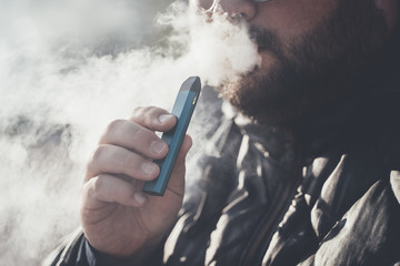 Man smokes new Vape Pod System, inhales and exhales vapor of electronic cigarette, vaping concept