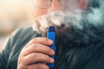 Man smokes new Vape Pod System, inhales and exhales vapor of electronic cigarette, vaping concept