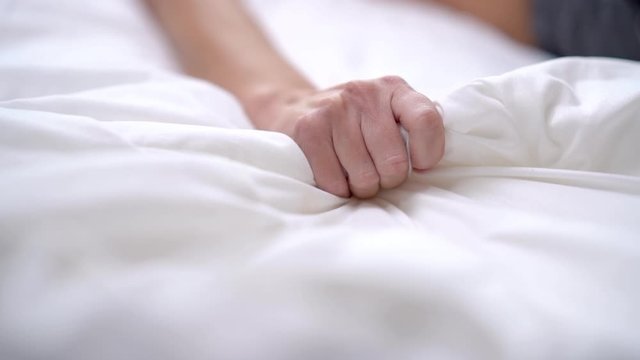 Woman's hand squeezing white sheet in erotic excitement