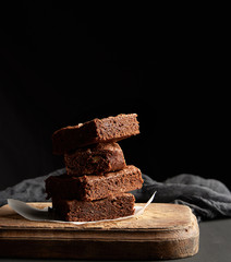 stack of baked square pieces of chocolate brownie cake on brown wooden cutting board
