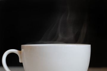 hot steam from the white cup with coffee drink on the dark background
