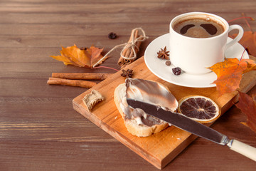 Cup of black coffee ,  autumn maple leaves, cinnamon, star anise, piece of dried orange, knife; wooden background,