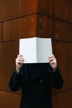 Man with book at face level near building