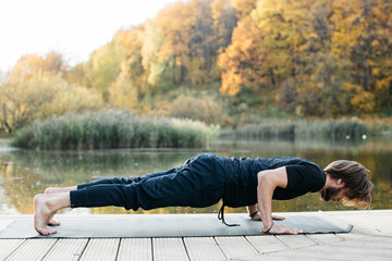 Young man doing yoga asana in the nature with the lake view. Evening workout outdoors, sports and healthy lifestyle