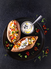 Baked sweet potato or yam, stuffed with chickpeas, rice, vegetables, red chilli pepper and yogurt sauce dressing. Top view, dark background with copy space. Healthy vegan food concept.