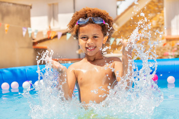Cute curly boy splash water in small swimming pool